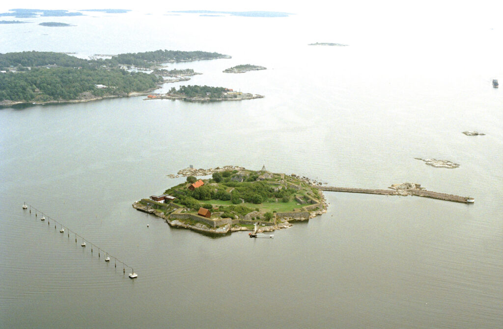 En lite blek bild från 90-talet med vy över havet . I mitten en ö med byggnader och runt om ön en mur.