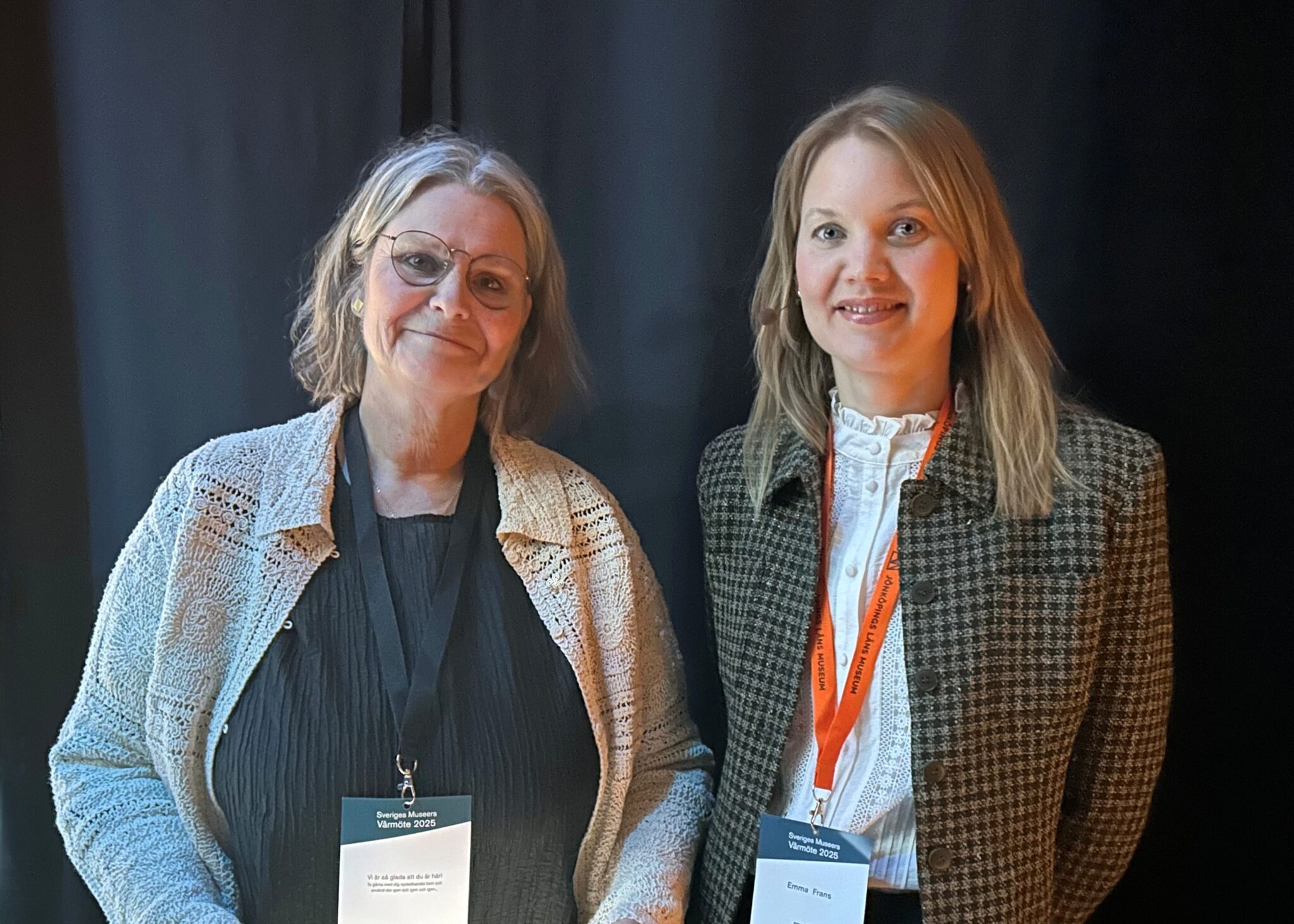 Två kvinnor med konferenskort kring halsen tittar in i kameran.
