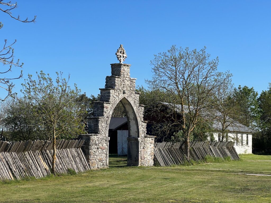 Porten till gården som välkomnar besökare är byggd av sten i trappstegsform med ett ringkors överst.
