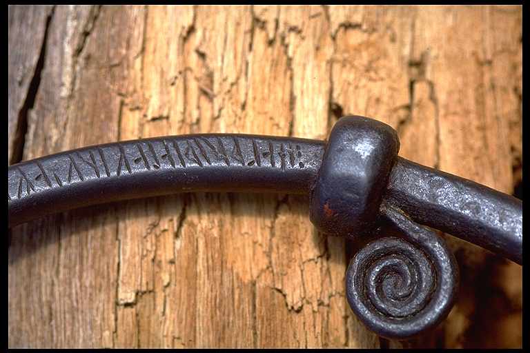 Närbild på detalj i runt handtag med inristade runor.