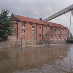 Tegelbyggnad i tre våningar speglar sig i vattenkanten.