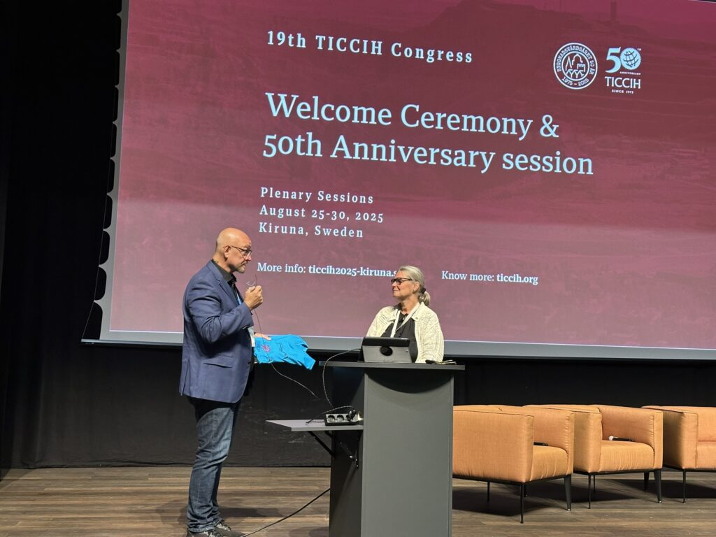 En man med blå kavaj står på en scen och talar i en mikrofon tillsammans med en en kvinna i vir kavaj.