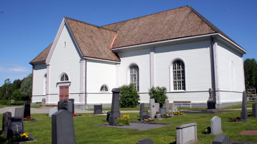 Vitputsad kyrka med trätak och romanska fönster.