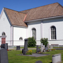 Vitputsad kyrka med trätak och romanska fönster.