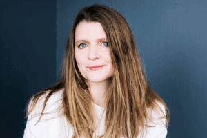 Porträtt på kvinna med långt brunt hår mot en blå bakgrund.