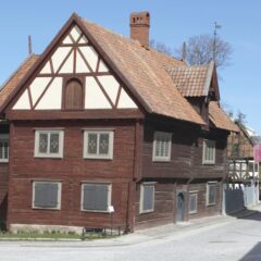 Rött trähus i två våningar med vita korsvirkesgavlar och rikt dekorerade fönster.