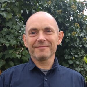 Porträtt på man, blå skjorta, ute, grönska i bakgrunden.