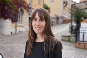 Porträttbild på kvinna med mörkt långt hår. Ute. Stadsmiljö.