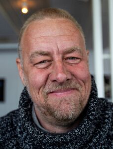 Närbild på man som ler och tittar in i kameran.