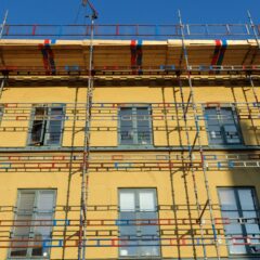 Fasad på äldre byggnad med gul puts och klädd i byggnadsställningar.