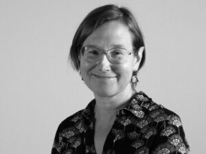 Svartvitt porträtt på kvinna med page och glasögon som ler och tittar in i kameran.