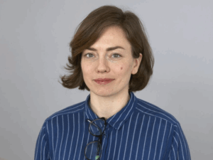 Porträtt, kvinna, mörkt, kort hår. Randig skjorta. Grå bakgrund.