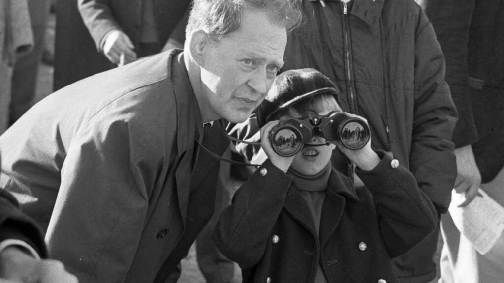 Pojke tittar i kikare, bredvid en vuxen man.