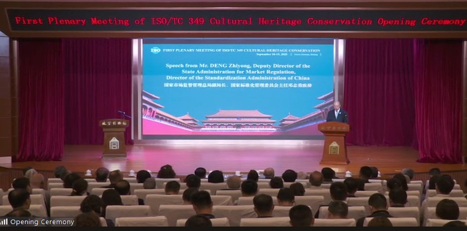 En sal med flera åhörares nackar. Längst fram en scen med en blå skärm och kinesisk och engelsk text.