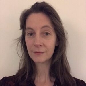 Porträtt av en kvinna med axellångt mörkt hår, mörk kavaj. Inne, ljus bakgrund.