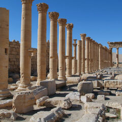 Vy över förstört tempel med tiotalet kolonner i rad med massor av nedrasade stenar bredvid.