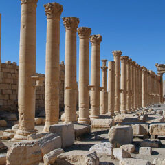 Vy över förstört tempel med tiotalet kolonner i rad med massor av nedrasade stenar bredvid.