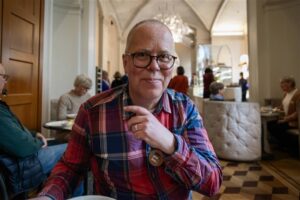 Porträtt, man, glasögon och rutig skjorta sittande vid ett bord i cafémiljö.