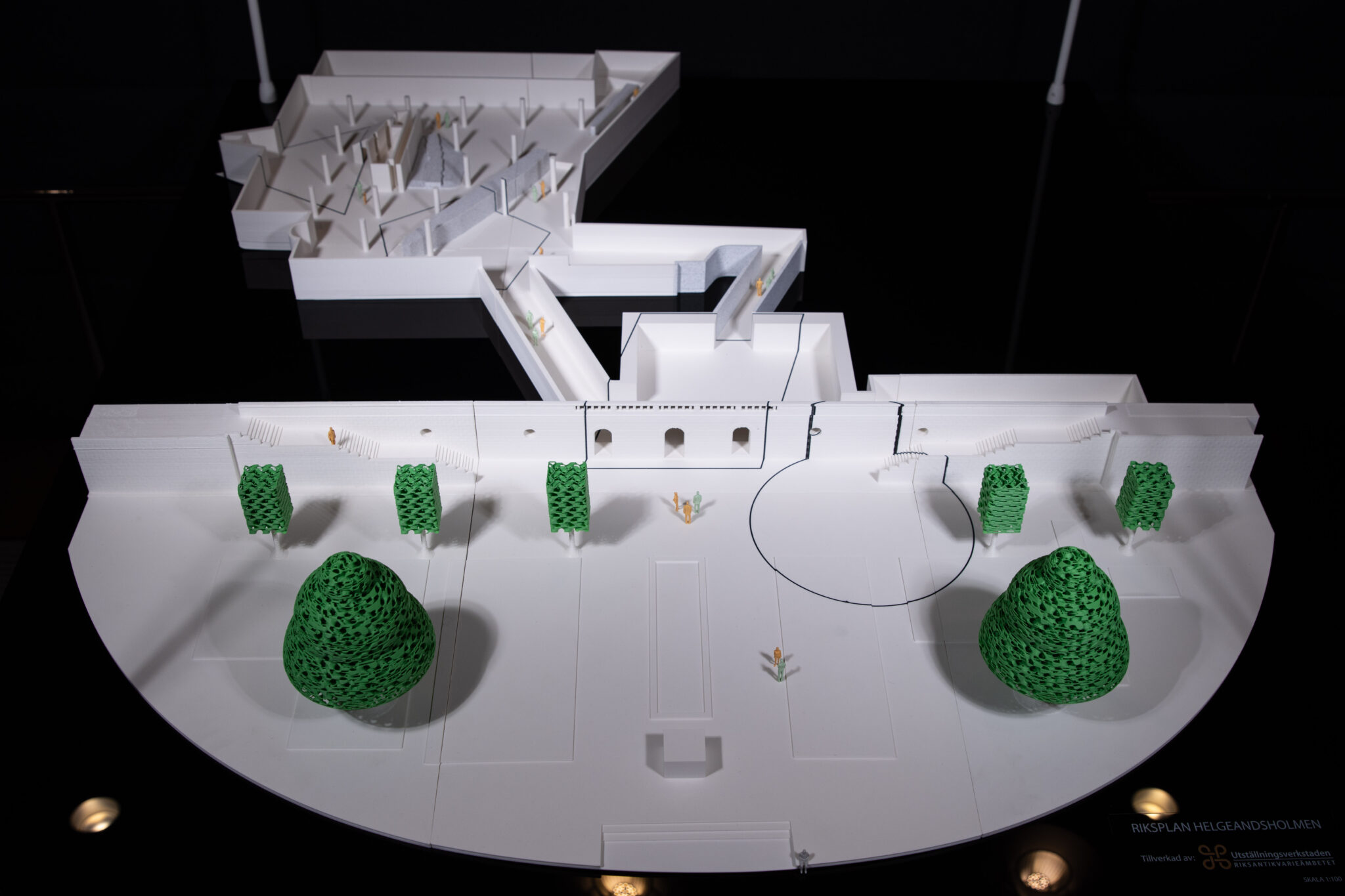 Detaljerad arkitektonisk modell som visar en byggnad med omgivande landskap. Modellen innehåller strukturer, gångvägar och gröna områden som representeras av texturerade element, troligen träd eller buskar.
