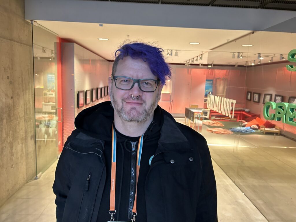 Man med glasögon och lila hår framför museilokal