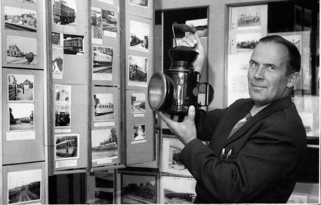 Svartvitt foto där en man håller upp en lådkamera med stor blixt. På väggen en fotoutställning.