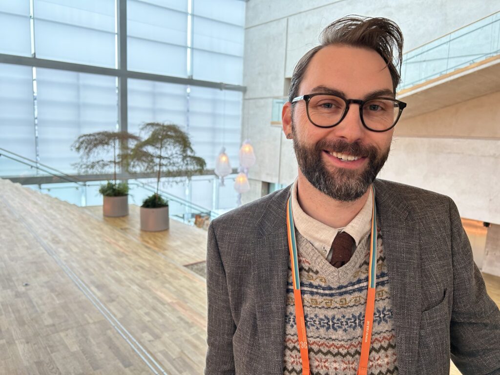 Leende man med skägg och glasögon framför stort fönster