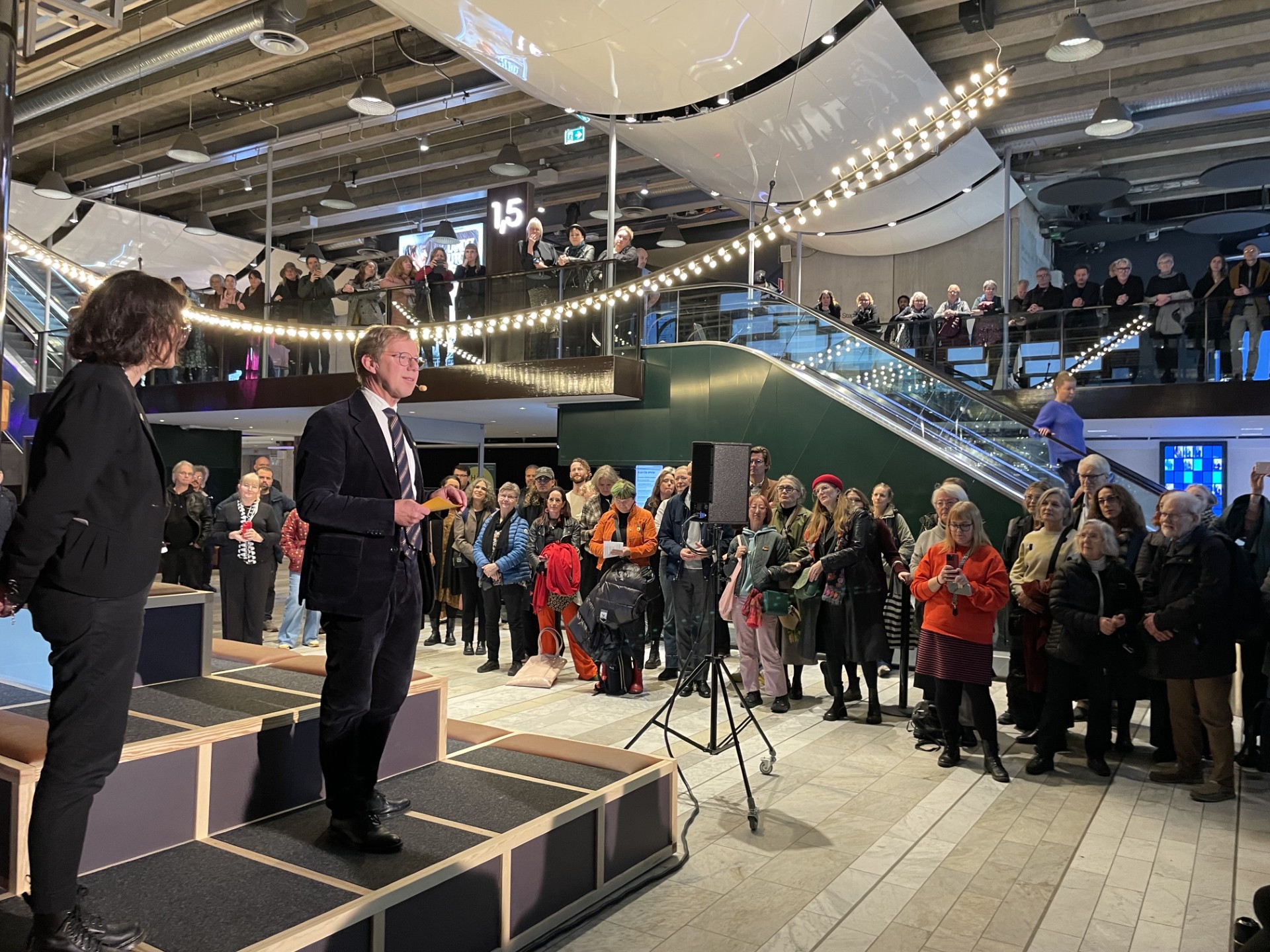 Två personer står på en scen och talar inför en publik