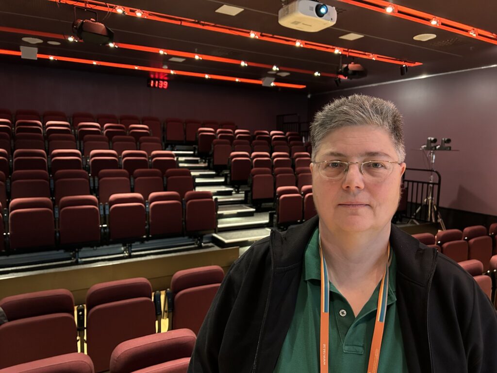 Kvinna med glasögon framför rader med stolar