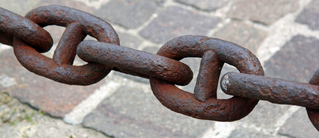 Stora rostiga länkar i en kedja som hänger över en stndlagd gata.