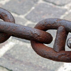 Stora rostiga länkar i en kedja som hänger över en stndlagd gata.
