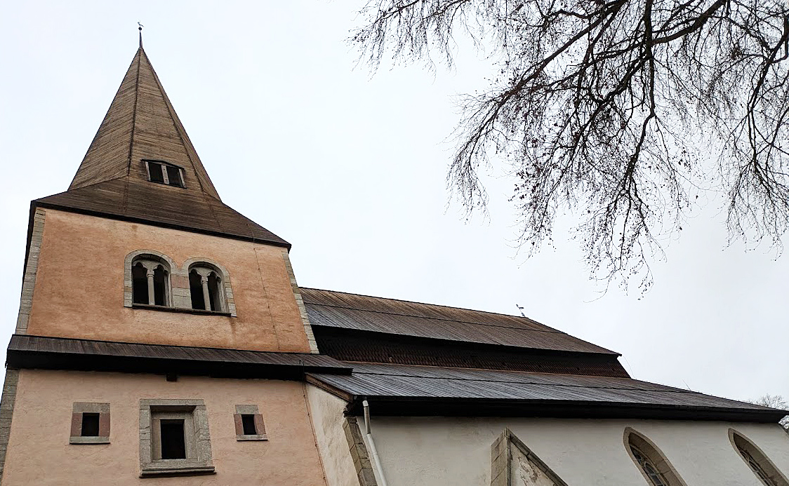 Exteriör av kyrka med högt torn och välvda fönster, nakna trädgrenar i förgrunden.