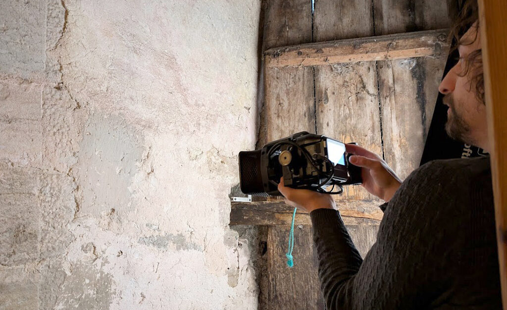Person fotograferar en gammal trädörr och väggen intill på nära håll.