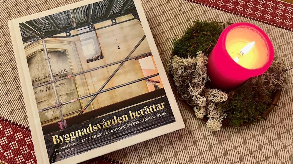 En bok ligger på ett bord med en julduk och ett tänt stearinljus.