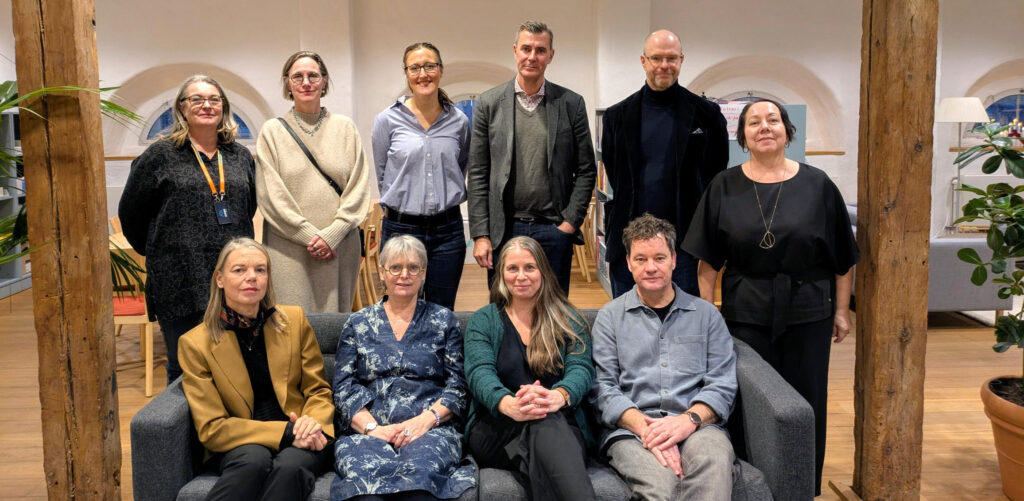 Tio personer står inomhus uppställda och tittar in i kameran