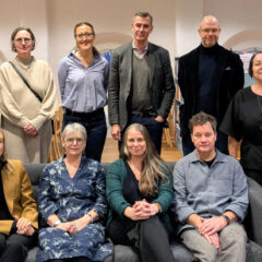 Tio personer står inomhus uppställda och tittar in i kameran