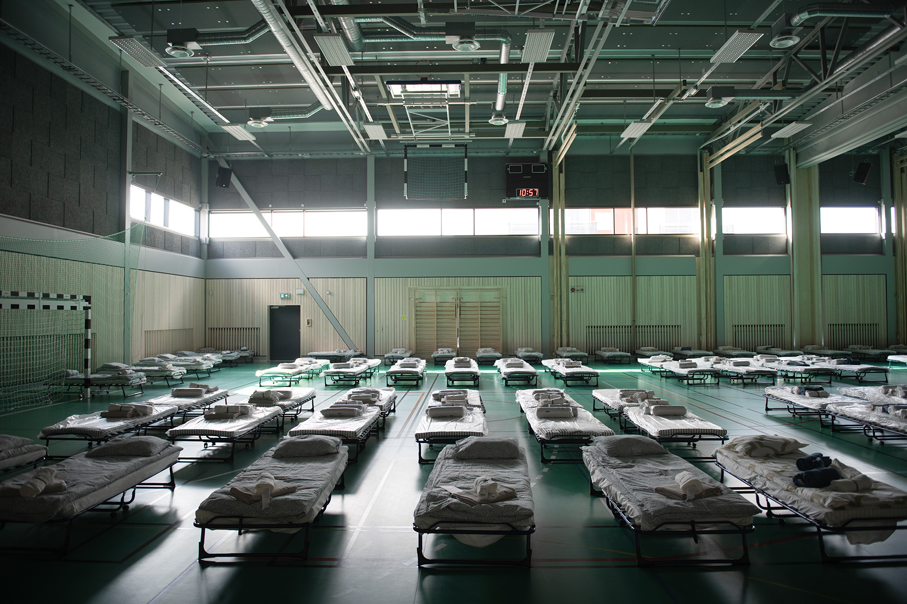 “Gymnastiksal med rader av bäddar och sängkläder, förberett som tillfälligt boende för flyktingar.”