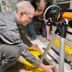 En man sitter på huk på golvet framför ett instrument där han placerar ett rostigt svärd.