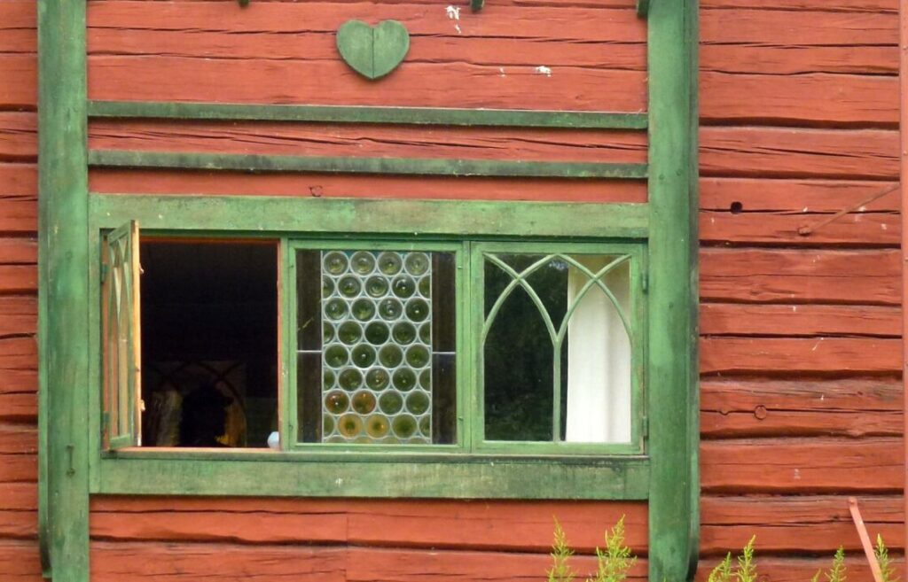 Fönster med gröna karmar mot rödmålade timmerväggar.