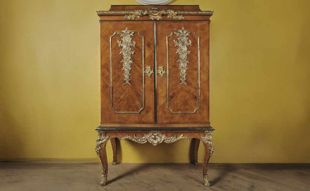 Ett träskåp med fyra ben och dekorationer på dörrarna.