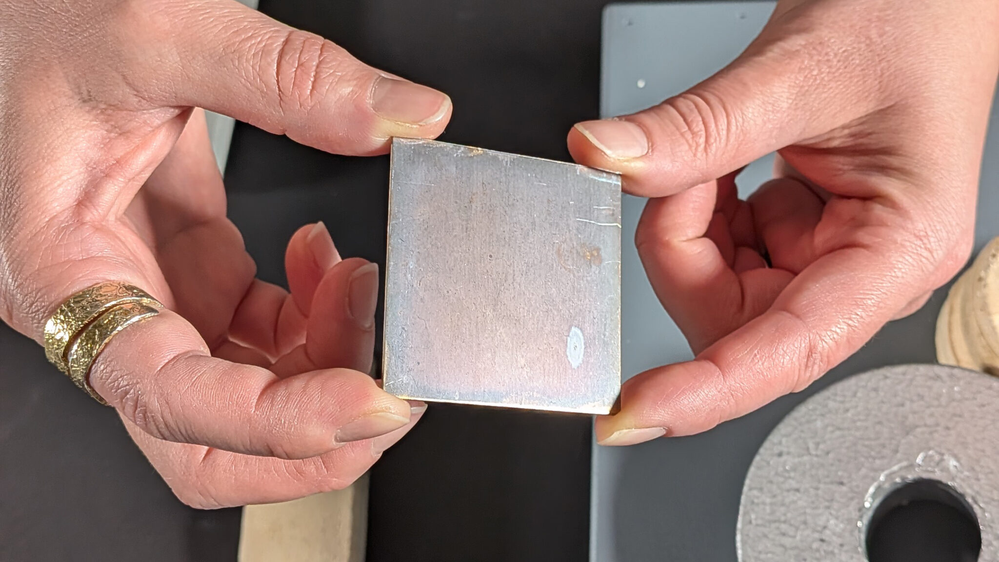 Närbild på två händer som håller en fyrkantig metallbit, 3-4 cm bredd.