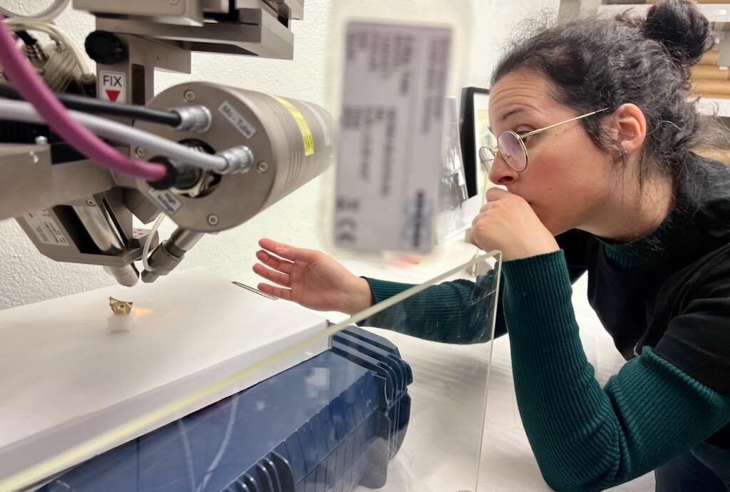 En ung kvinna lutar sig fram och placerar en glasskärva under en avancerad teknisk aparat.