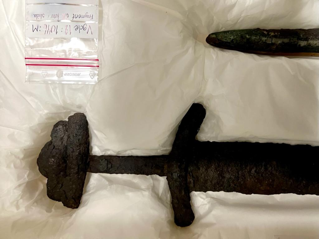 Ett rostigt svärd ligger varsamt placerad på ett mjukt underlag.