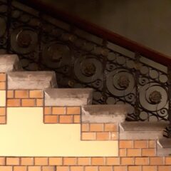 En trappa med utsirat räcke leder från höger upp mot vänster. Dekor av tegel och gul puts på sidan.