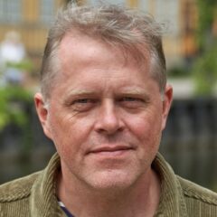 Porträttbild på ljushårig man i grön skorta med randig t-shirt under.