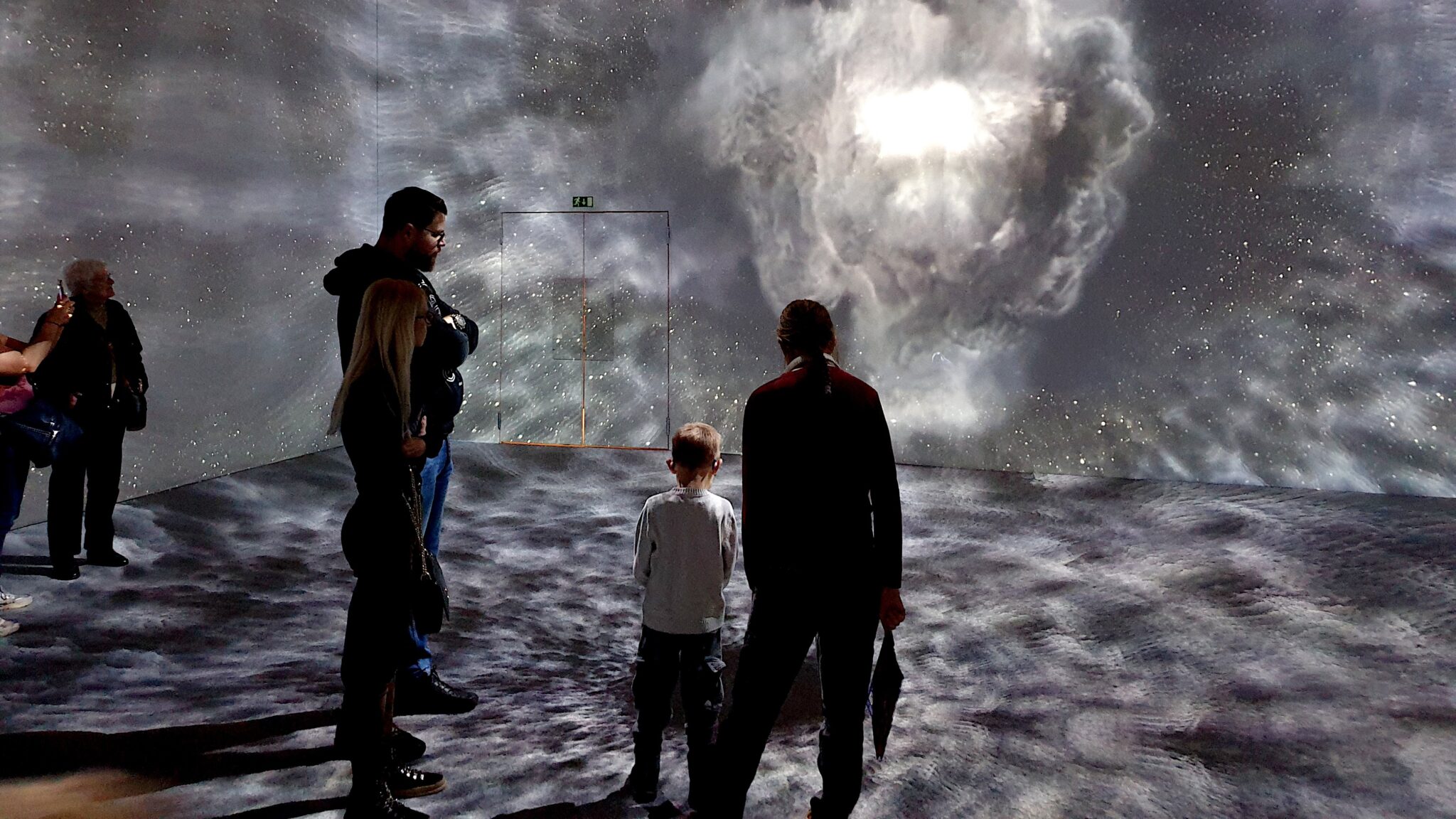 En grupp människor står i ett mörkt utställningsrum där projektioner visas på väggen.