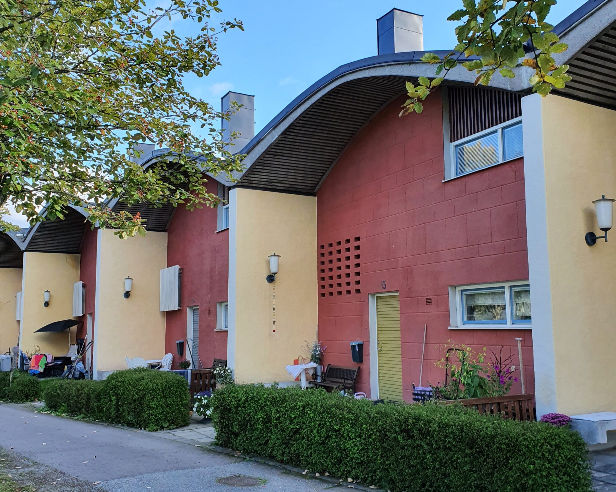 Radhuslänga längs en gata, röda putsade fasader med välvda tak och låga häckar framför.
