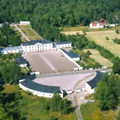 Flygbild över en herrgårdsanläggning omgiven av skog och åkermark, med huvudbyggnad, två flyglar och en stor öppen gårdsplan framför.