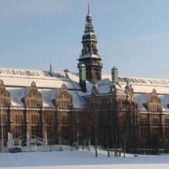 Alt‑text: Stor historisk byggnad med fasad i kalk- och sandsten och med snötäckta tak och torn i vinterljus.