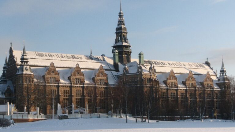 Alt‑text: Stor historisk byggnad med fasad i kalk- och sandsten och med snötäckta tak och torn i vinterljus.