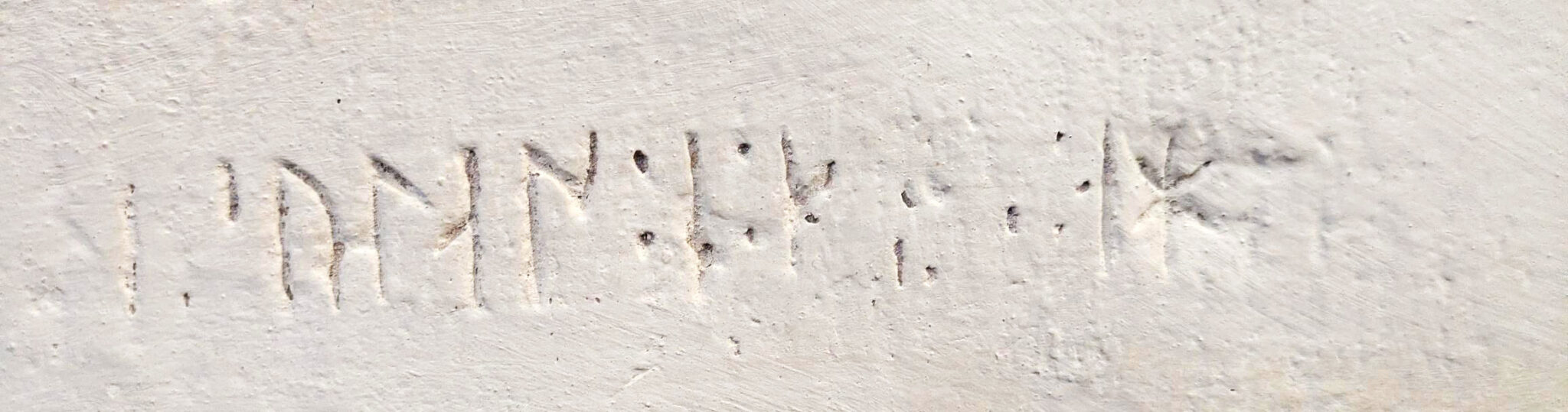 En närbild av en ljus vägg med inristade tecken eller symboler.